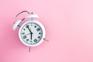 White alarm clock on the pink surface top view copy space