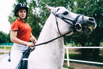 Female jockey riding purebred stallion near fence