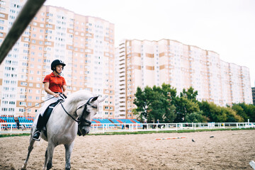 Young female jockey in black helmet riding horse on sand paddock