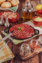 Grilled brazilian sausage on iron plate with bread, salad, farofa and spices - Linguiça