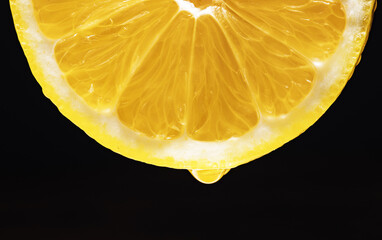 Juicy slice of yellow lemon with a drop of juice.