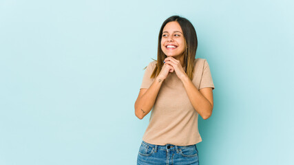 Young woman isolated on blue background keeps hands under chin, is looking happily aside.
