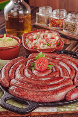 Grilled brazilian sausage on iron plate with salad, farofa and spices - Linguiça close-up