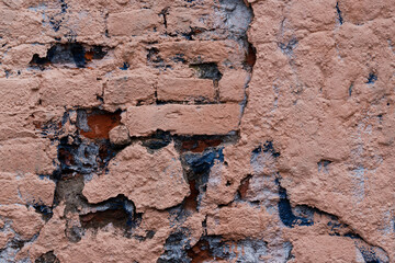 Old brick wall with peeling stucco. Weathered rough wall surface with brickwork. The wall is painted in different colors. Vintage background. Urban texture.