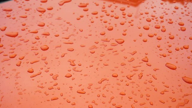 Dolly handheld shot for water droplets on har hood orange smooth surface during the day