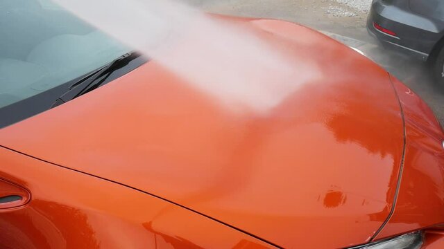 High pressure water pistol streams water on orange car's hood during a carwash Service 
