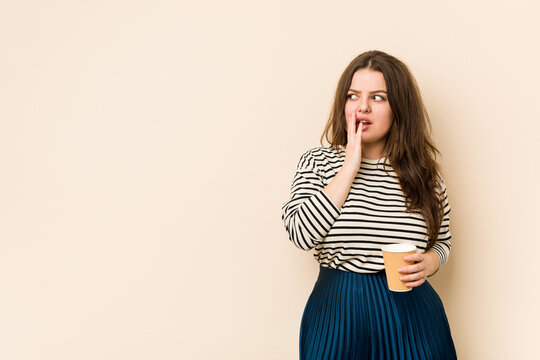 Young curvy woman holding a coffee is saying a secret hot braking news and looking aside