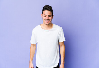 Young caucasian man isolated on purple background laughs and closes eyes, feels relaxed and happy.