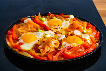 Shakshuka - fried eggs with salmon and vegetables in frying pan
