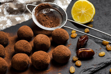 Homemade vegan truffles with dried fruits, walnuts and raw cocoa powder served on black slate plate.