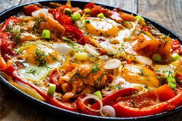 Shakshuka - fried eggs with salmon and vegetables in frying pan
