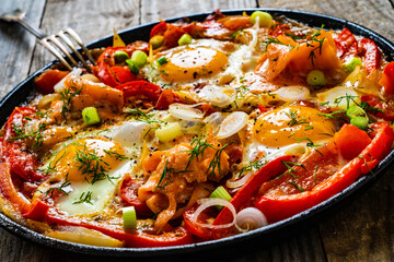 Shakshuka - fried eggs with salmon and vegetables in frying pan
