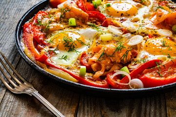Shakshuka - fried eggs with salmon and vegetables in frying pan

