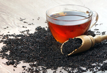 a cup of black tea and dry black tea leaves on a wooden table