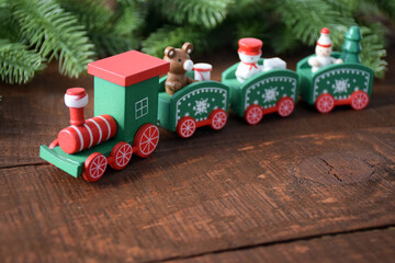 Colorful Christmas train with pine tree branches on old brown rustic pine wooden board as texture or background for design. New Year 2021, Merry Christmas frame template with copy space.