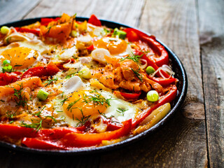 Shakshuka - fried eggs with salmon and vegetables in frying pan

