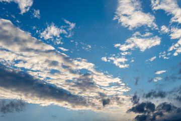 Summer blue sky with dramatic clouds. Sunlit clouds during sunset as a background