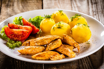 Chicken nuggets with boiled potatoes and vegetables on wooden table
