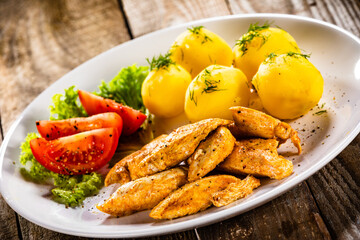 Chicken nuggets with boiled potatoes and vegetables on wooden table
