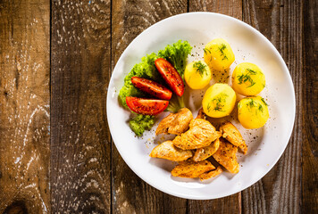 Chicken nuggets with boiled potatoes and vegetables on wooden table
