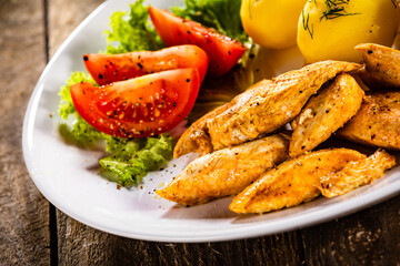 Chicken nuggets with boiled potatoes and vegetables on wooden table
