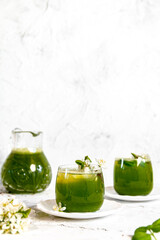 Green basil lemonade with yellow lemon and  white flowers on white painted background