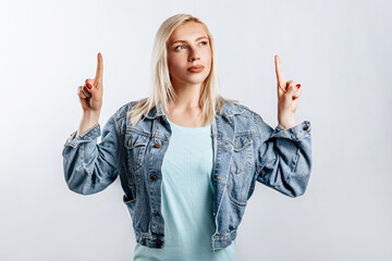 Look here. Young beautiful blonde woman points her fingers to the top thinks and makes a decision. The woman thought about the choice. Place for advertising.