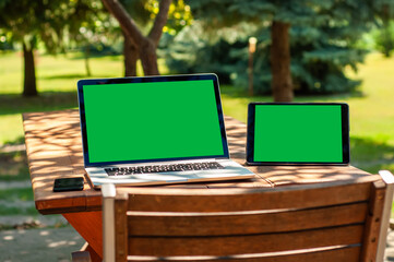 View on a laptop pc and a smartphone and a tablet pc with a green screen on a table in the garden