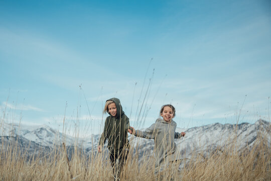 Two children running in a field holding hands