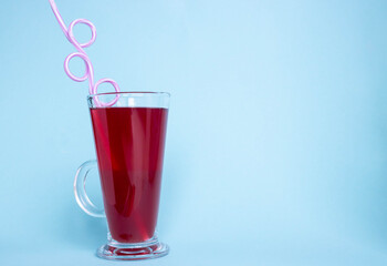 A glass with strawberry juice and a curved tube on a blue background. Space for your text