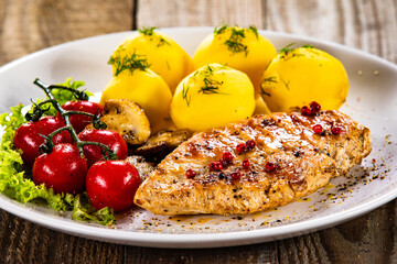 Fried chicken breast with boiled potatoes and fresh vegetables on wooden table