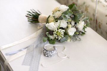 Bride jewelry bracelet and stylish modern wedding bouquet in white and gray colors on a table in the bedroom.