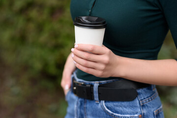 Young woman in outdoors holds a white paper tumbler in her hands with coffee or tea. Close-up shot....