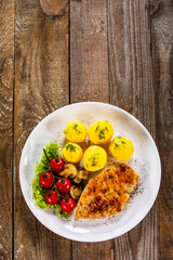 Fried chicken breast with boiled potatoes and fresh vegetables on wooden table