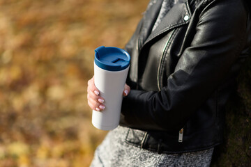 Woman in a leather jacket outdoors hold a eco friendly reusable coffee mug. Take coffee with a reusable travel mug. Zero waste. Sustainable lifestyle concept.