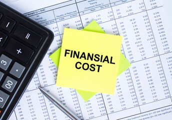Sticker with text Financial Cost lying on the financial tables. Calculator with metal pen