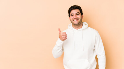 Young man isolated on beige background smiling and raising thumb up