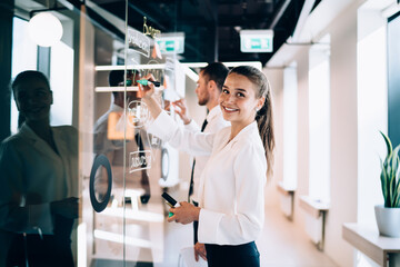 Young female office worker writing on wall and smiling