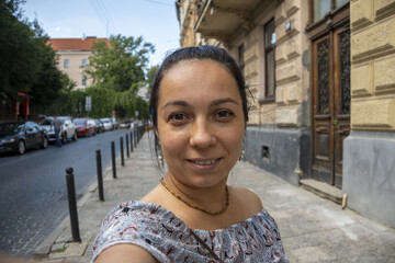 Street portrait of a woman 35-40 years old looking directly into the camera on a neutral background of the old city. She may be communicating via video link on the phone.