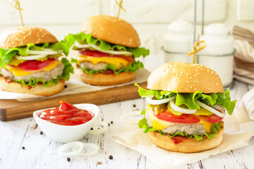 Delicious burgers, hamburger sandwich with cutlet, cheese, bacon and tomatoes on a wooden table.