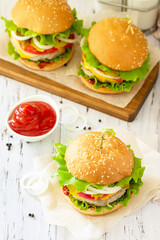 Delicious burgers, hamburger sandwich with cutlet, cheese, bacon and tomatoes on a wooden table.