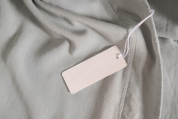 Clothing paper tag on ligh gray fabric. Fashion brand name mock up, closeup, top view, copy space for text - 375956725