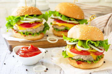 Delicious burgers, hamburger sandwich with cutlet, cheese, bacon and tomatoes on a wooden table.