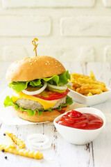 Delicious homemade burgers with cutlet, cheese, bacon, tomatoes and french fries on a wooden table. Copy space.