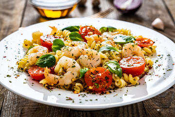 Pasta with prawns and vegetables highly seasoned on wooden table