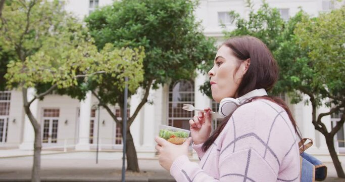 Young Caucasian woman eating and walking