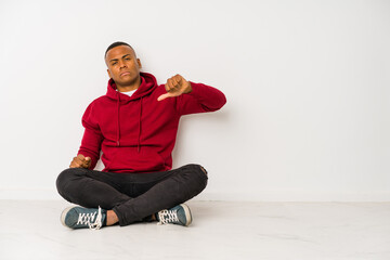 Young latin man sitting on the floor isolated showing a dislike gesture, thumbs down. Disagreement concept.