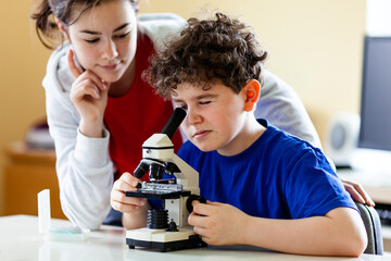 Girl and boy examining preparation under the microscope
