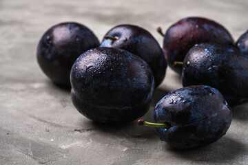 Fresh ripe plum fruits with water drops on stone concrete background, angle view macro
