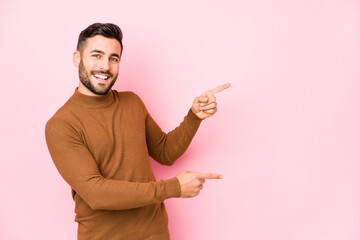 Young caucasian man against a pink background isolated excited pointing with forefingers away.